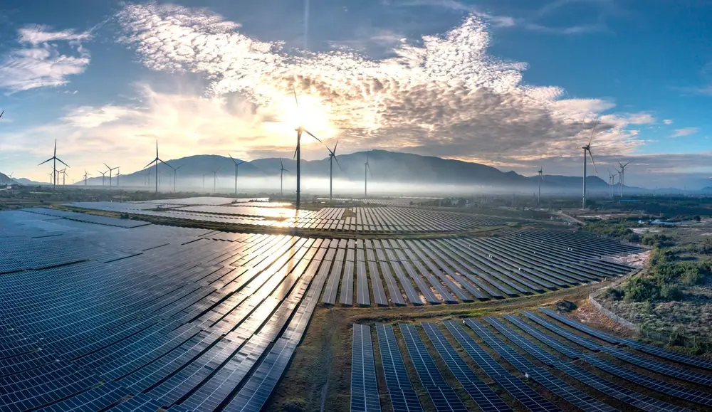 Aerial view of a solar farm and wind turbines at sunrise